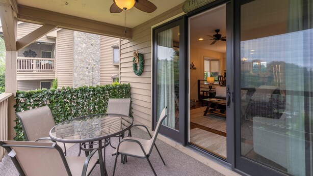 A covered patio with a glass table and chairs, a ceiling fan, and a sliding glass door leading to an interior dining area.