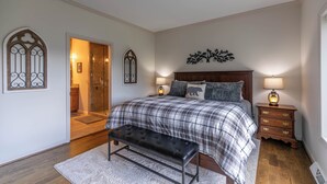 A bedroom with a bed, bench, bedside tables, and a door leading to a bathroom.