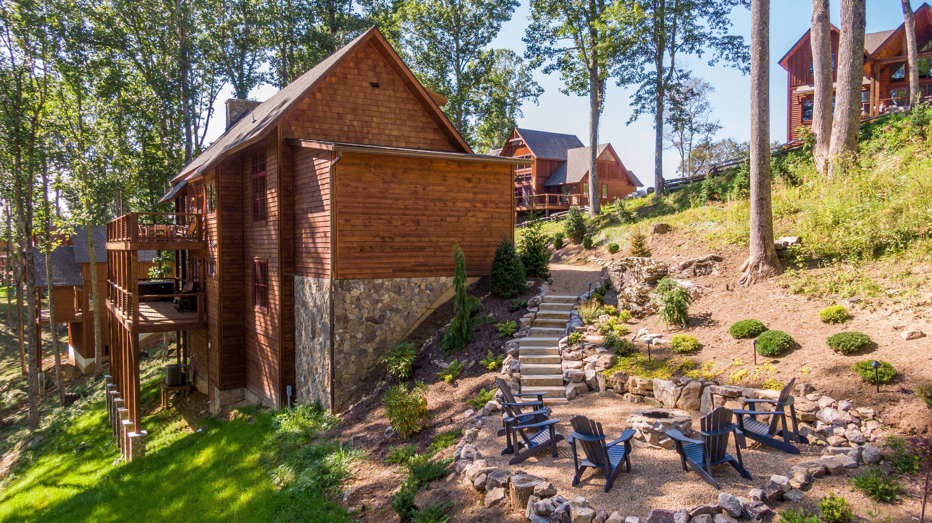 A wooden cabin with a stone foundation, a deck, and a fire pit area.