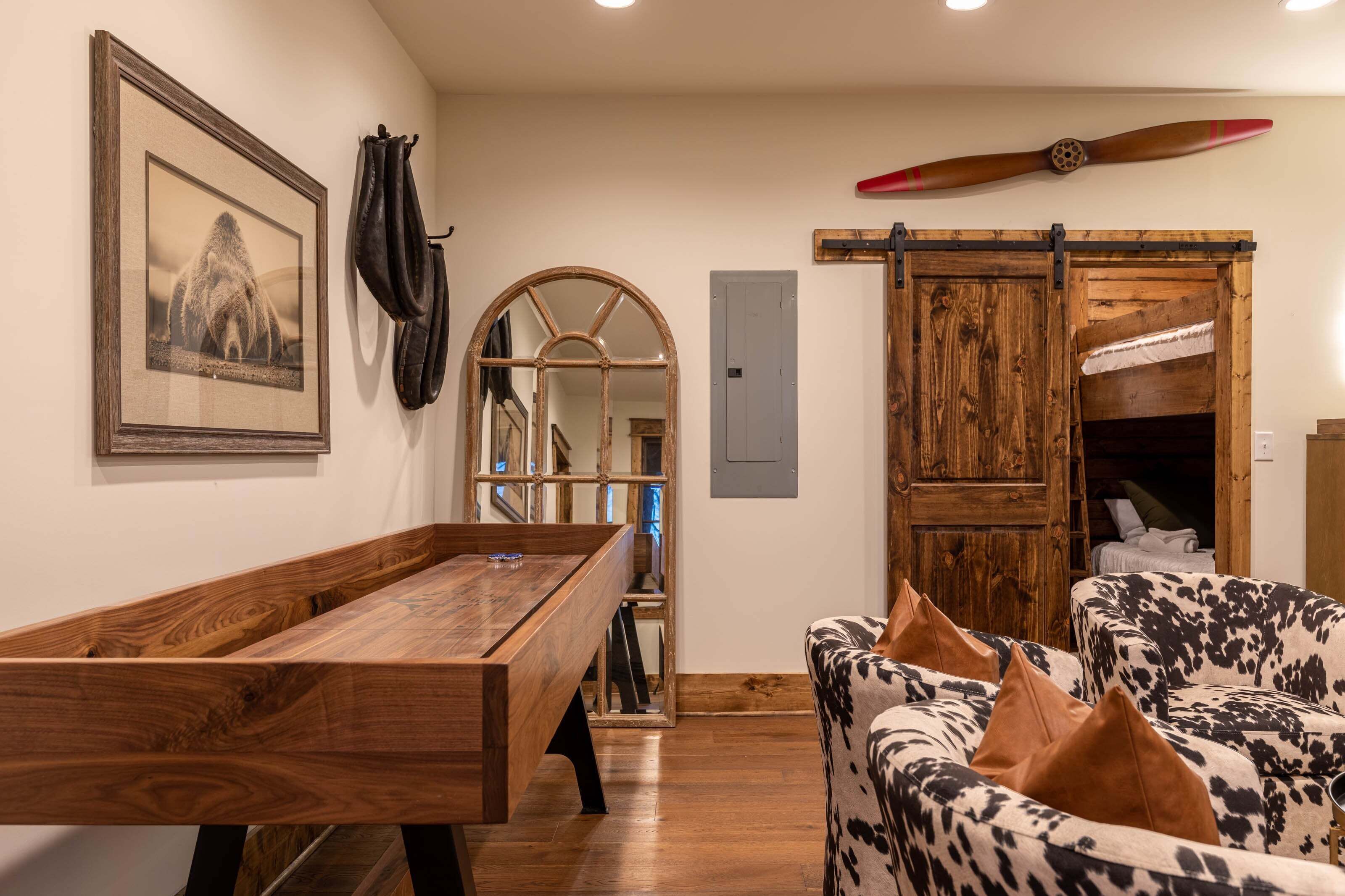 A wooden pool table, a cow print sofa, a mirror, a framed picture, and a wooden door with a propeller.