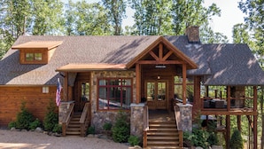 A rustic cabin with a stone exterior, wooden porch, and a chimney. - Tipsy Elk at Eagles Nest (Banner Elk)