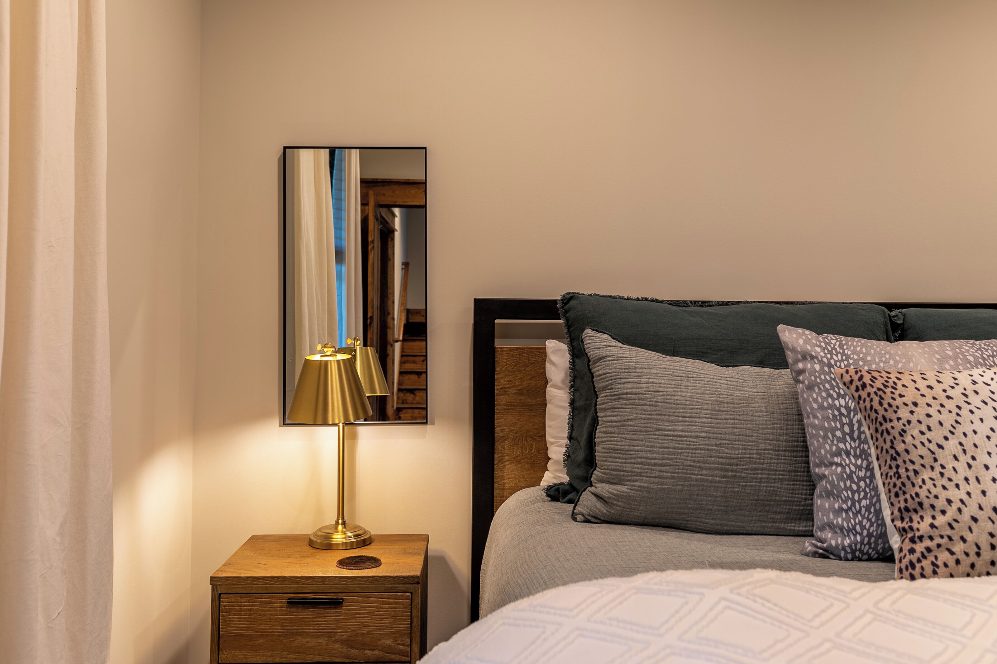 Une chambre bien rangée, avec un lit, une table de chevet dotée d’une lampe et un miroir au mur.
