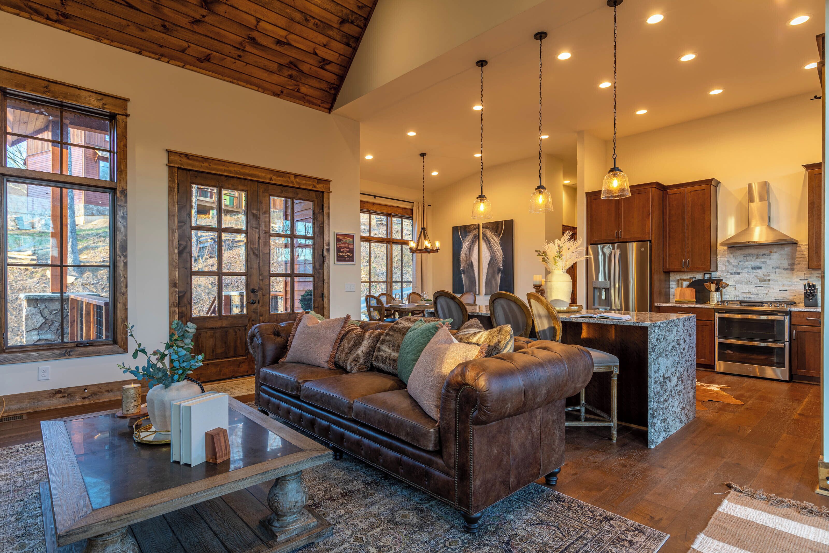 A spacious living room with a leather sofa, wooden ceiling, and large windows.