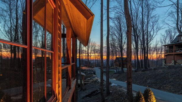 A wooden cabin with large windows, surrounded by trees and a clear sky. - Tipsy Elk at Eagles Nest (Banner Elk)