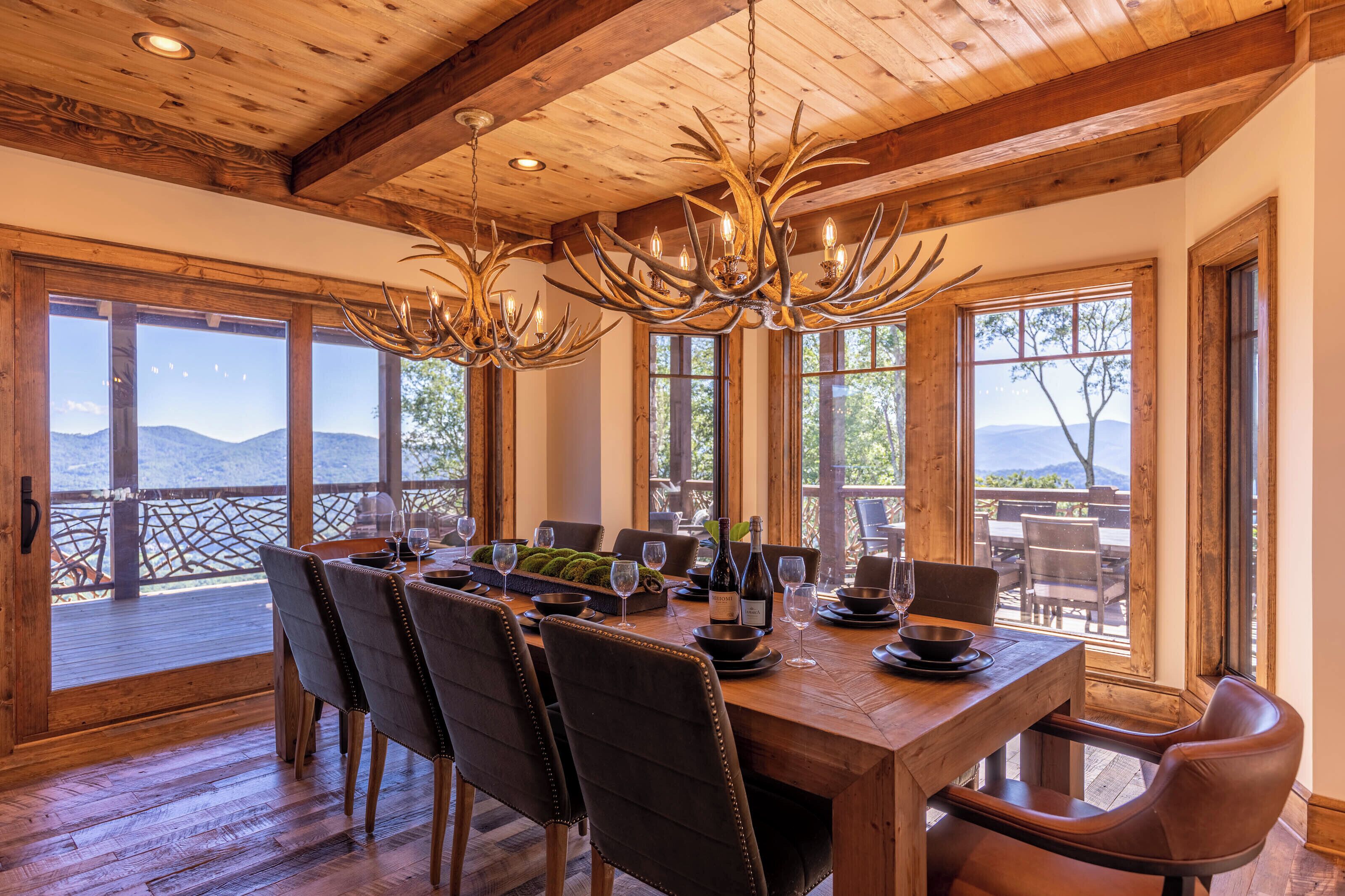 Comedor con mesa de madera dispuesta para seis personas, ventanas amplias y vistas a las montañas.