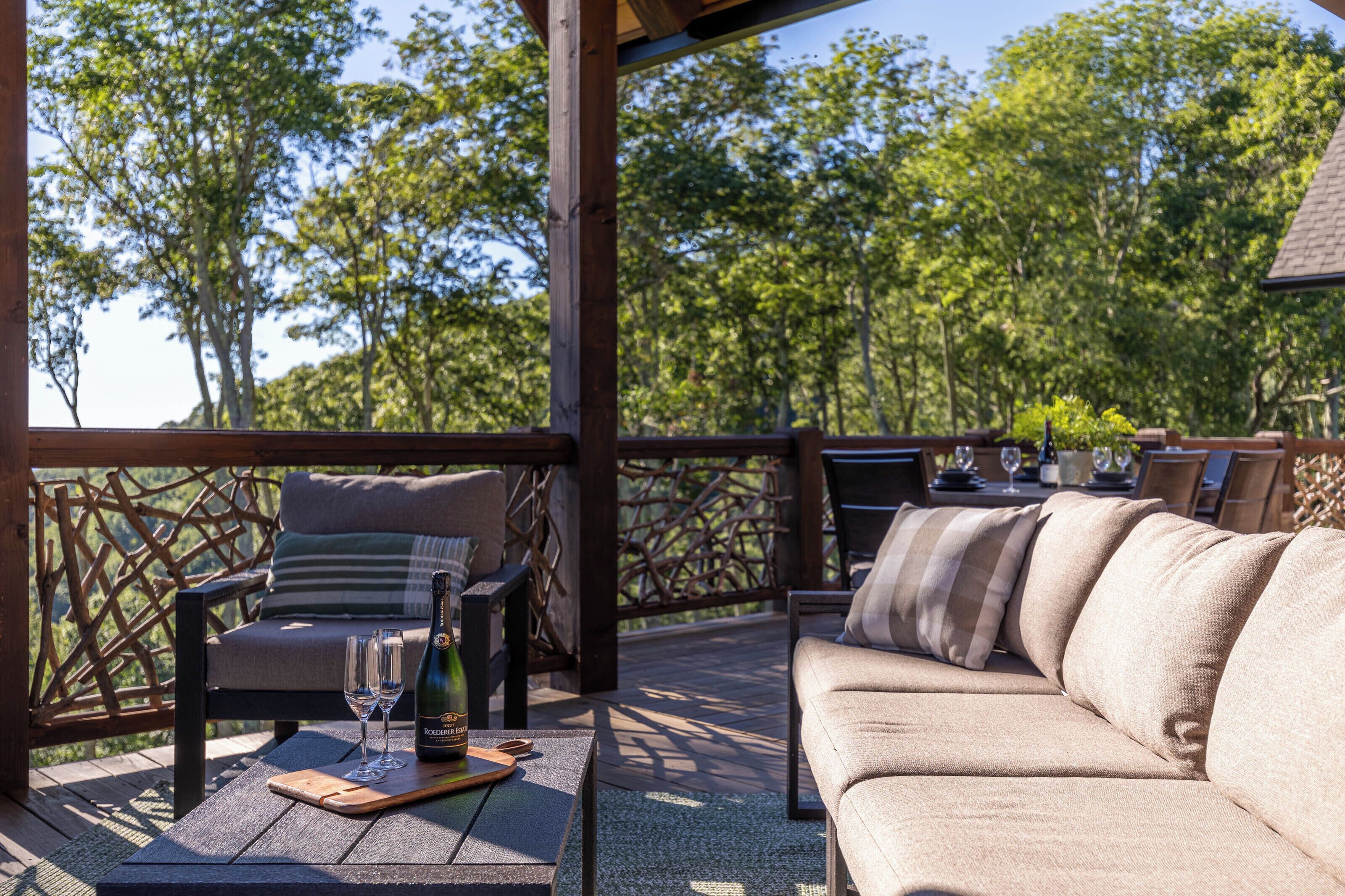 Une terrasse extérieure avec une plateforme en bois, un canapé confortable, une table en bois et une bouteille de vin.