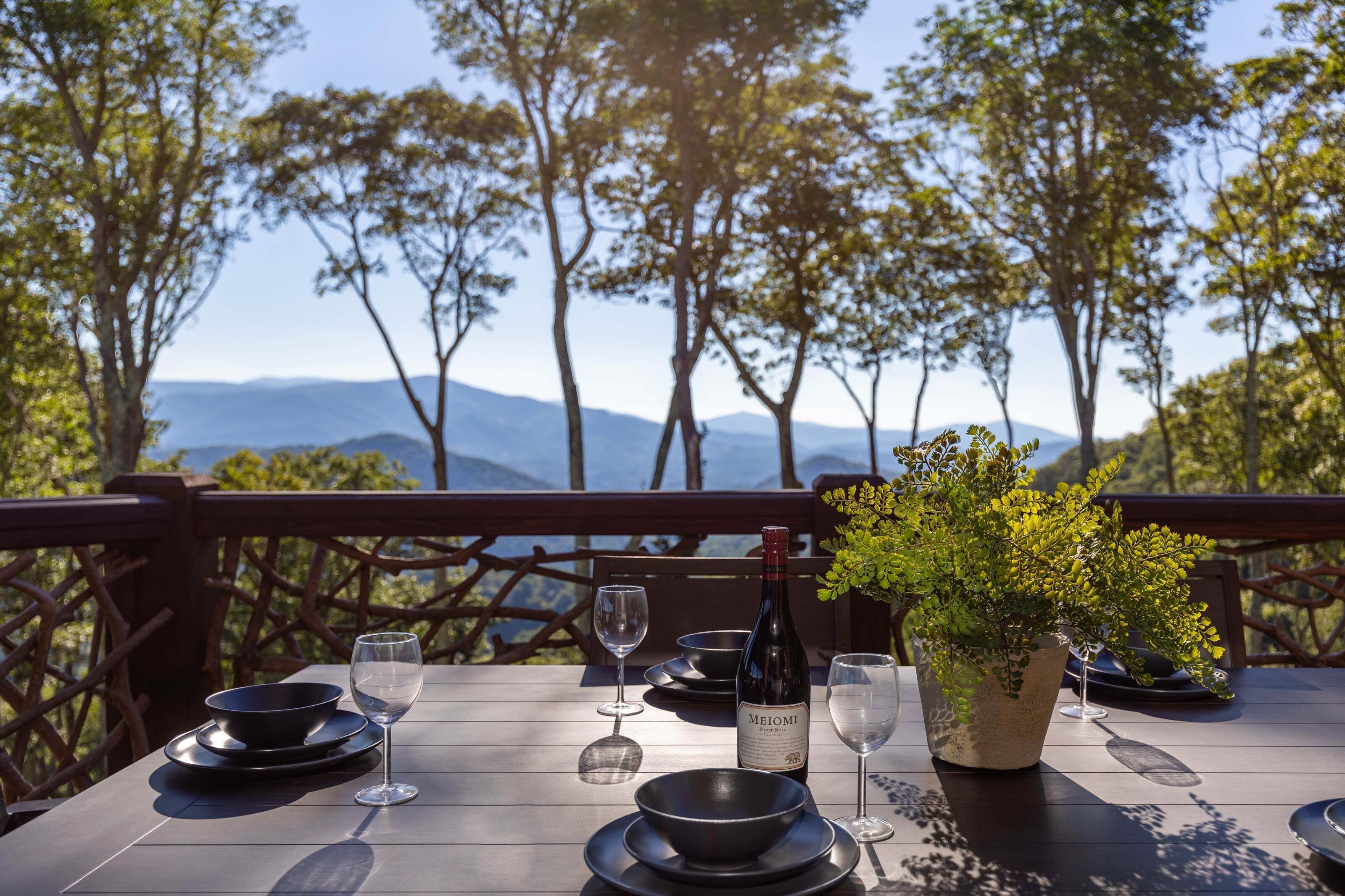 Mesa al aire libre con una botella de vino Meomi, copas, fuentes y una planta en maceta.