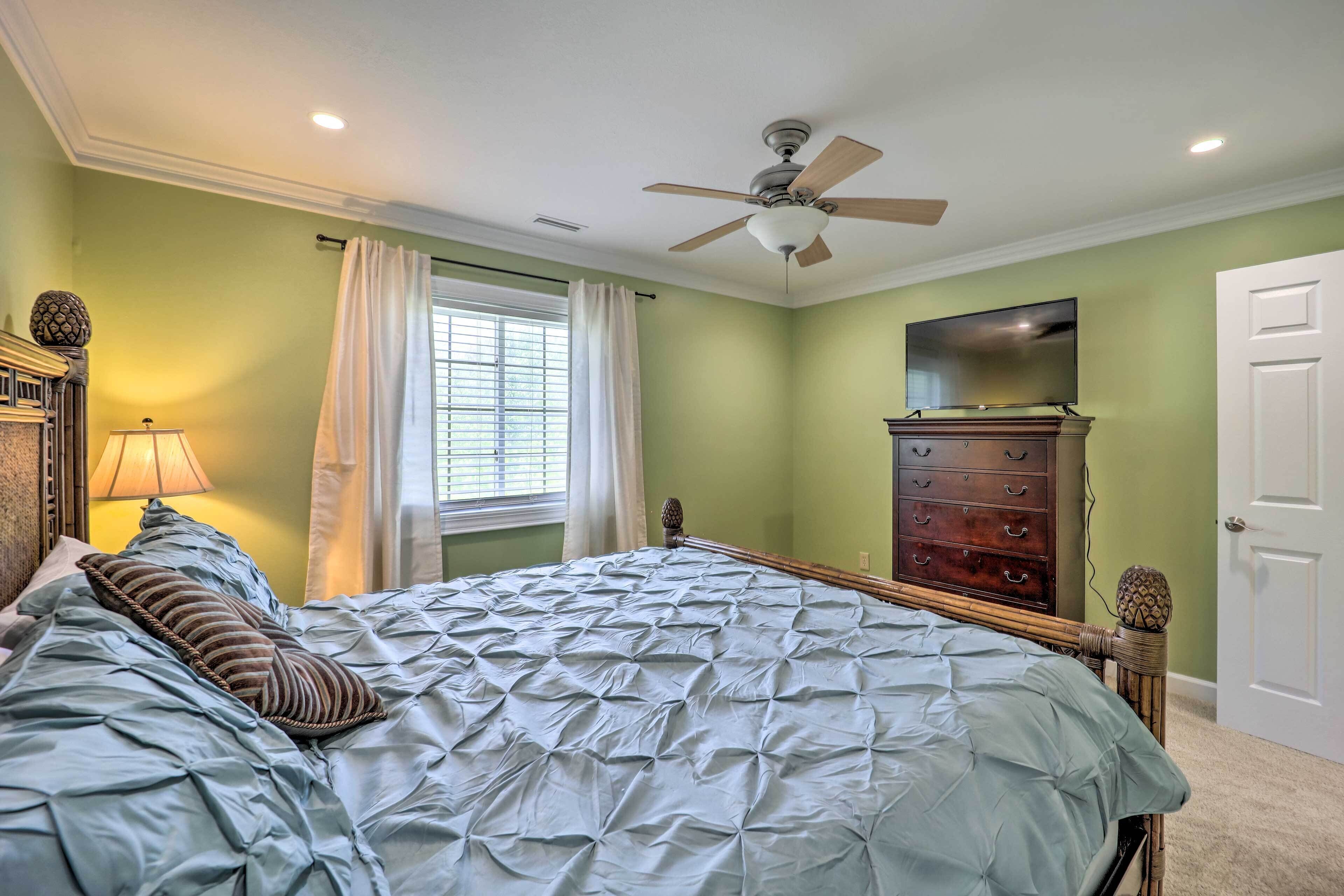 Une chambre à coucher comprenant un lit, un ventilateur de plafond, une commode et un téléviseur.