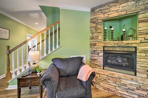 A living room with a stone fireplace, a staircase, and a grey armchair. - Lillys Mountain Escape (Banner Elk)