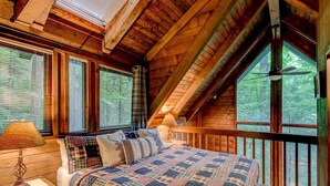 Une chambre avec un grand lit, une table de chevet, une lampe et une fenêtre donnant sur des arbres.