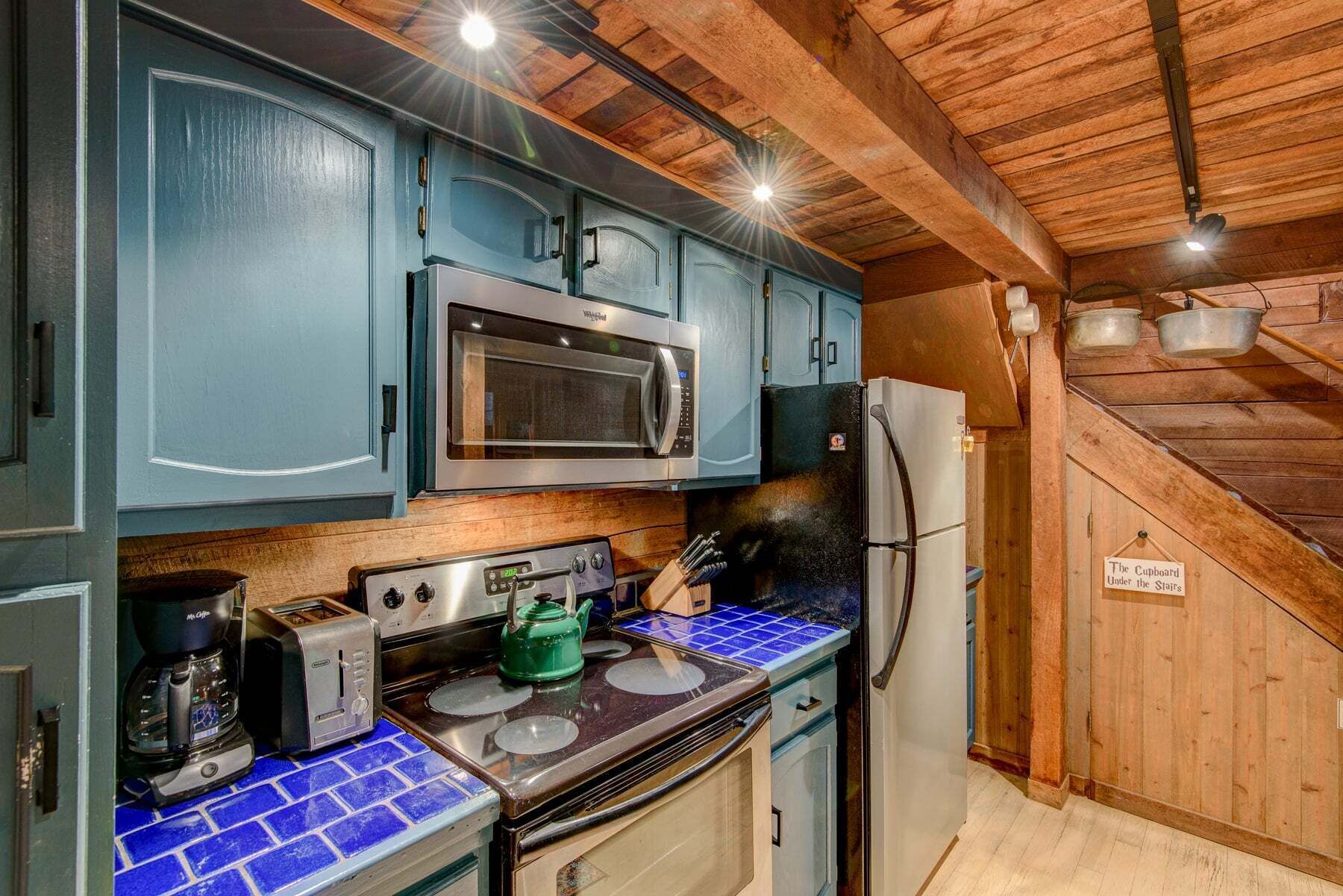 A compact kitchen with a microwave, toaster, kettle, and a refrigerator.