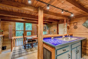 Ein rustikales Blockhaus-Interieur mit einer Essnische aus Holz, einer Küche mit blau gefliestem Spritzschutz und großen Fenstern mit Blick auf den Wald.