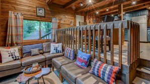 Un intérieur de chalet chaleureux avec un canapé, des coussins, une table basse et une vue sur l’extérieur.