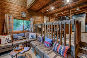 Ein gemütliches Blockhaus-Interieur mit einer Couch, Kissen, einem Couchtisch und Blick ins Freie.