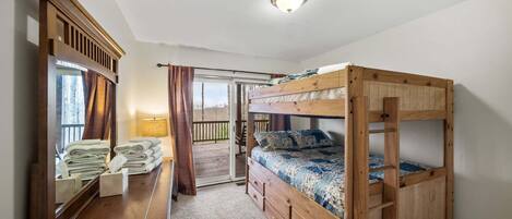 A bunk bed room with a wooden headboard, a mirror, a wooden dresser, and a view through a sliding door to an outdoor deck.