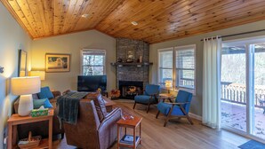 A cozy living room with a stone fireplace, wooden ceiling, and a television. - High Ground One Level House - Pet Friendly (Boone)