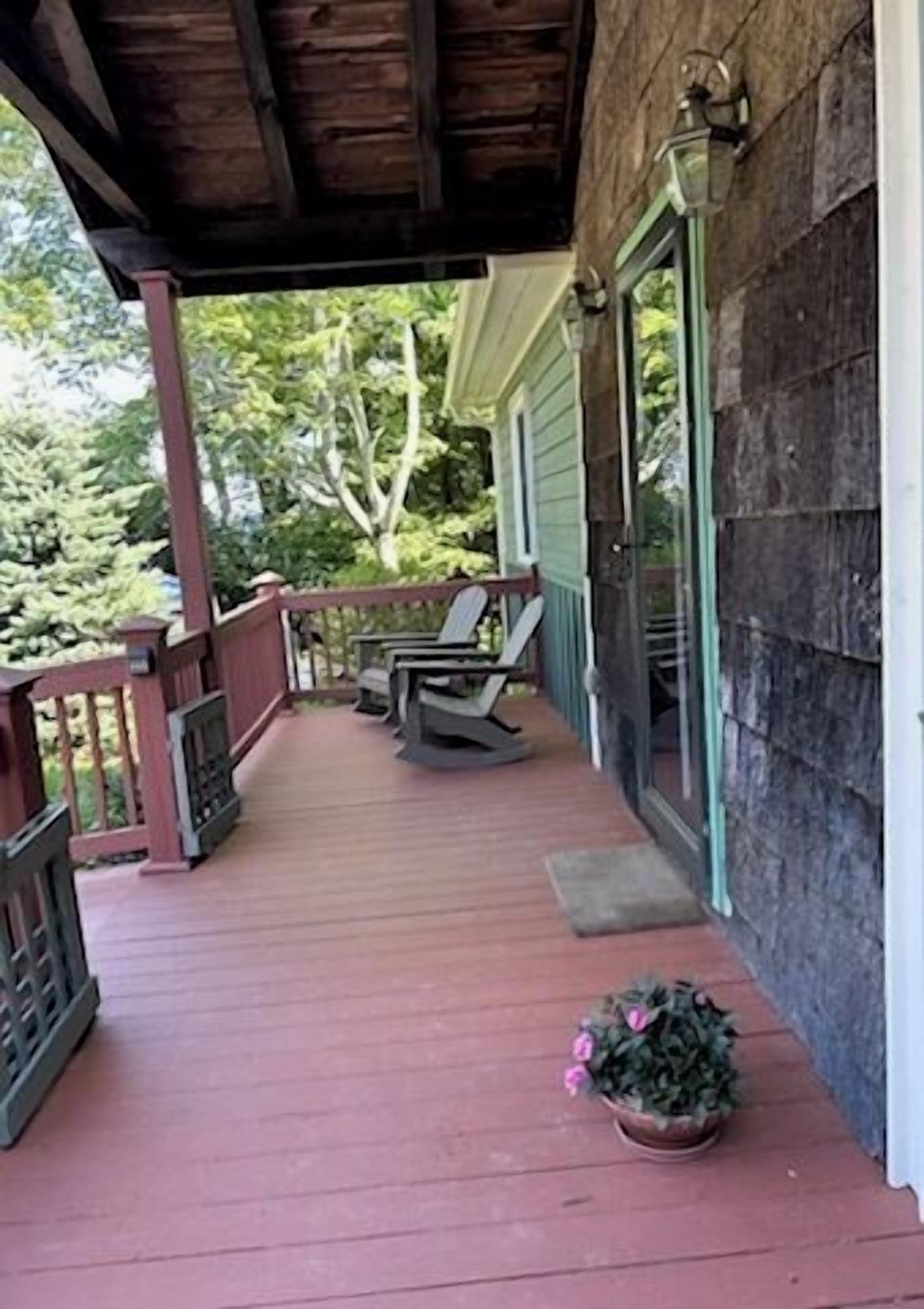 A wooden porch with a red floor, two chairs, and a potted plant.