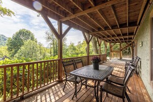 Una terraza techada al aire libre con barandas de madera, una mesa con sillas y vistas a un área boscosa.