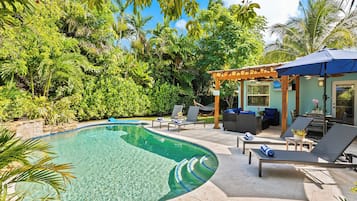 Piscina com espreguiçadeiras e årea de estar coberta, cercada por vegetação exuberante.