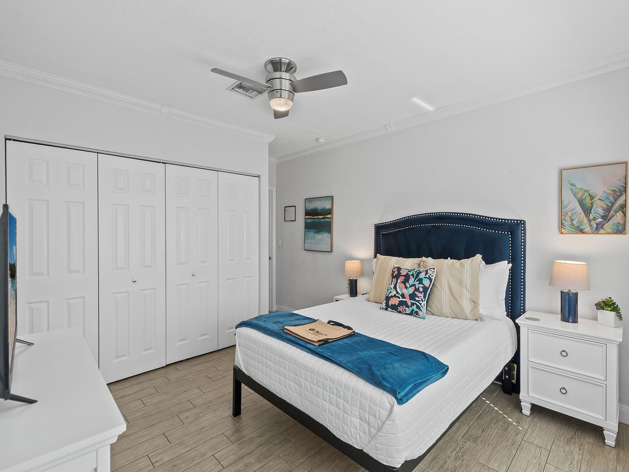 A bedroom with a bed, nightstands, a ceiling fan, and a wardrobe.