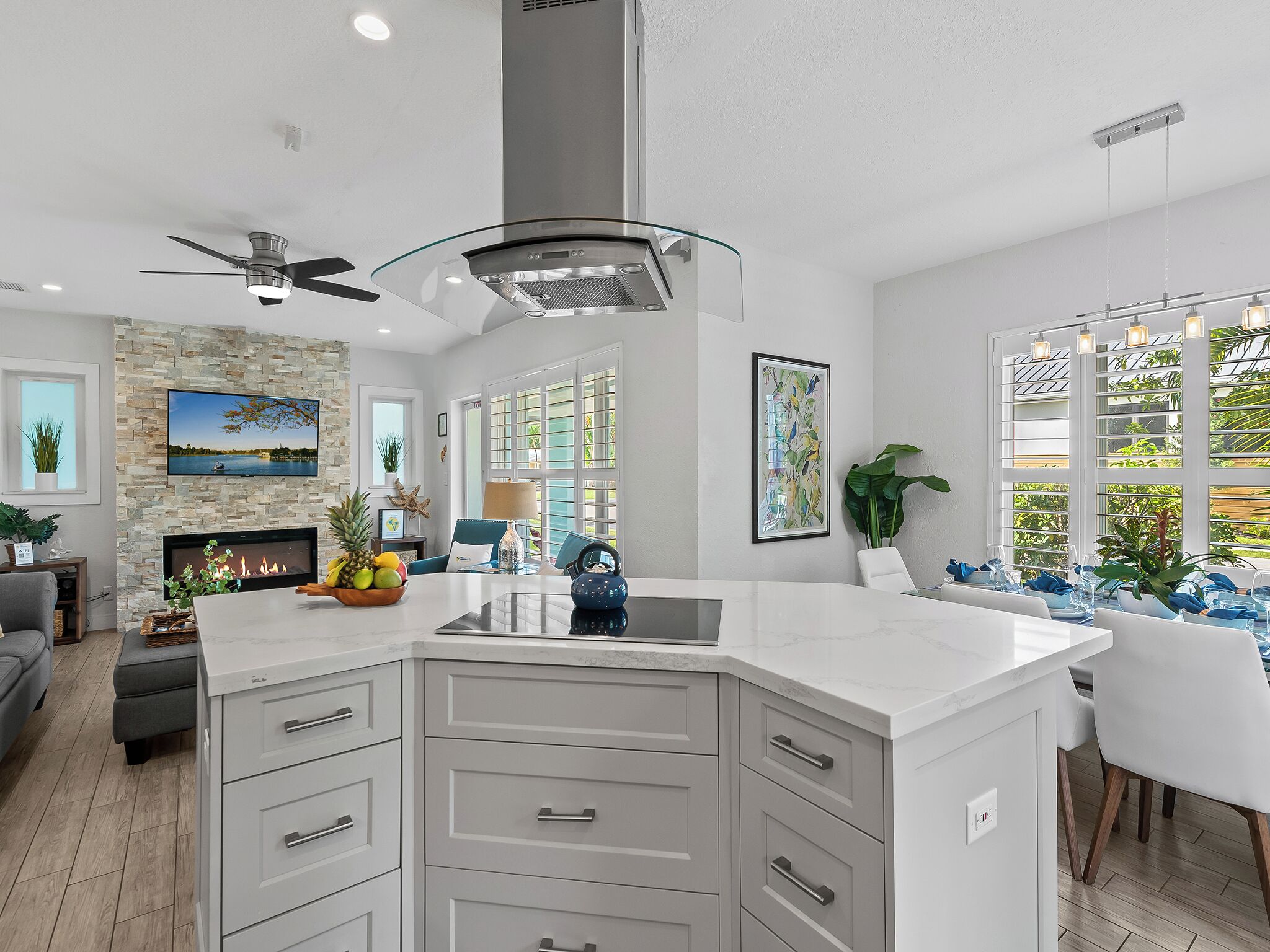 A modern kitchen with a large island, a fireplace, and a dining area with a view of greenery.