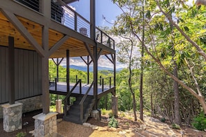 Eine Holzterrasse mit Steinunterbau, eine Treppe zu einem Balkon und ein Blick auf eine bewaldete Landschaft.