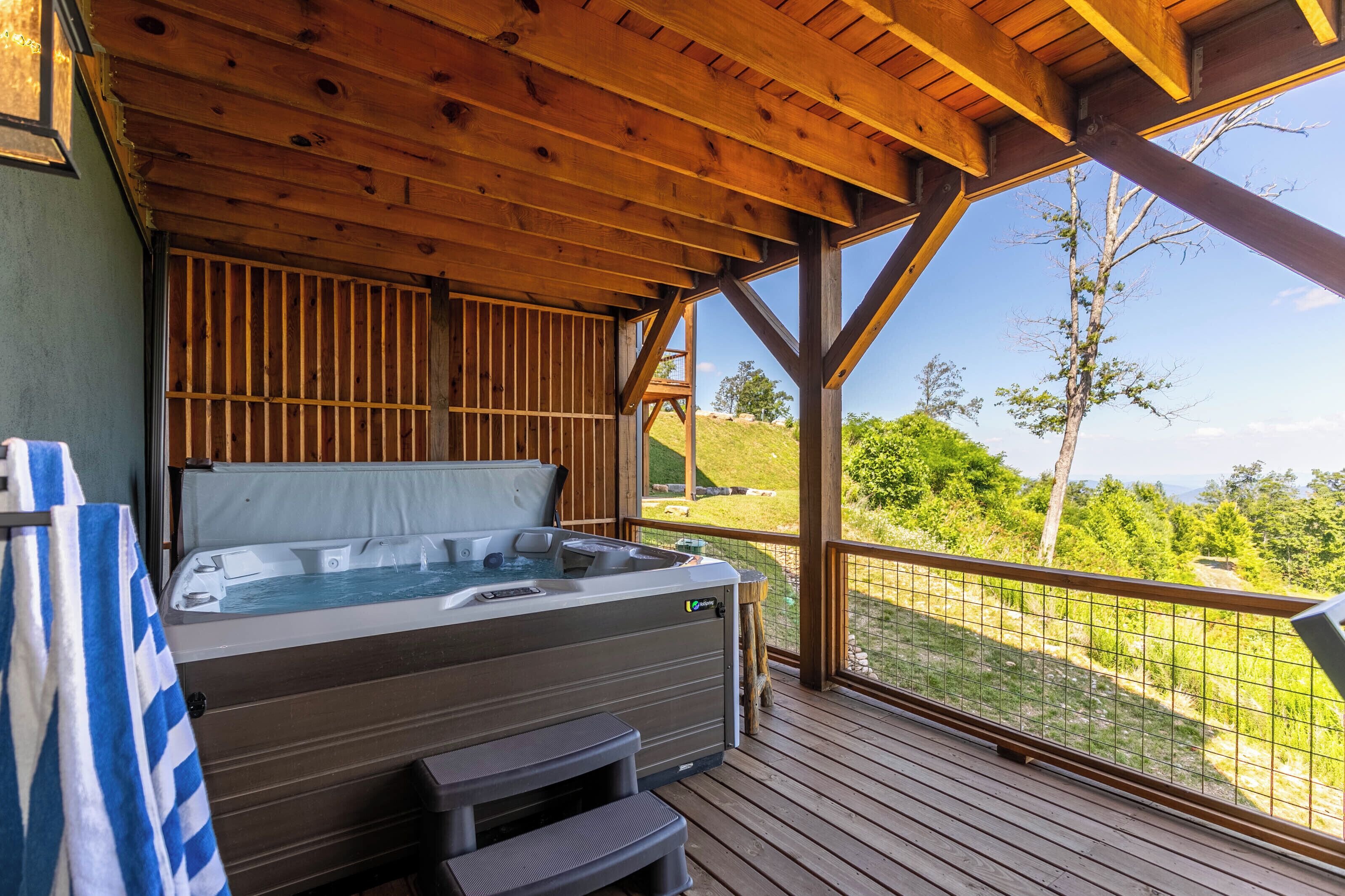 A hot tub on a wooden deck with a view of a grassy landscape and trees.