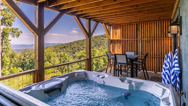 A wooden deck with a hot tub, outdoor seating, and a view of a forested mountain range. - Mountain Kandy at Blue Ridge Mountain Club (Lenoir)
