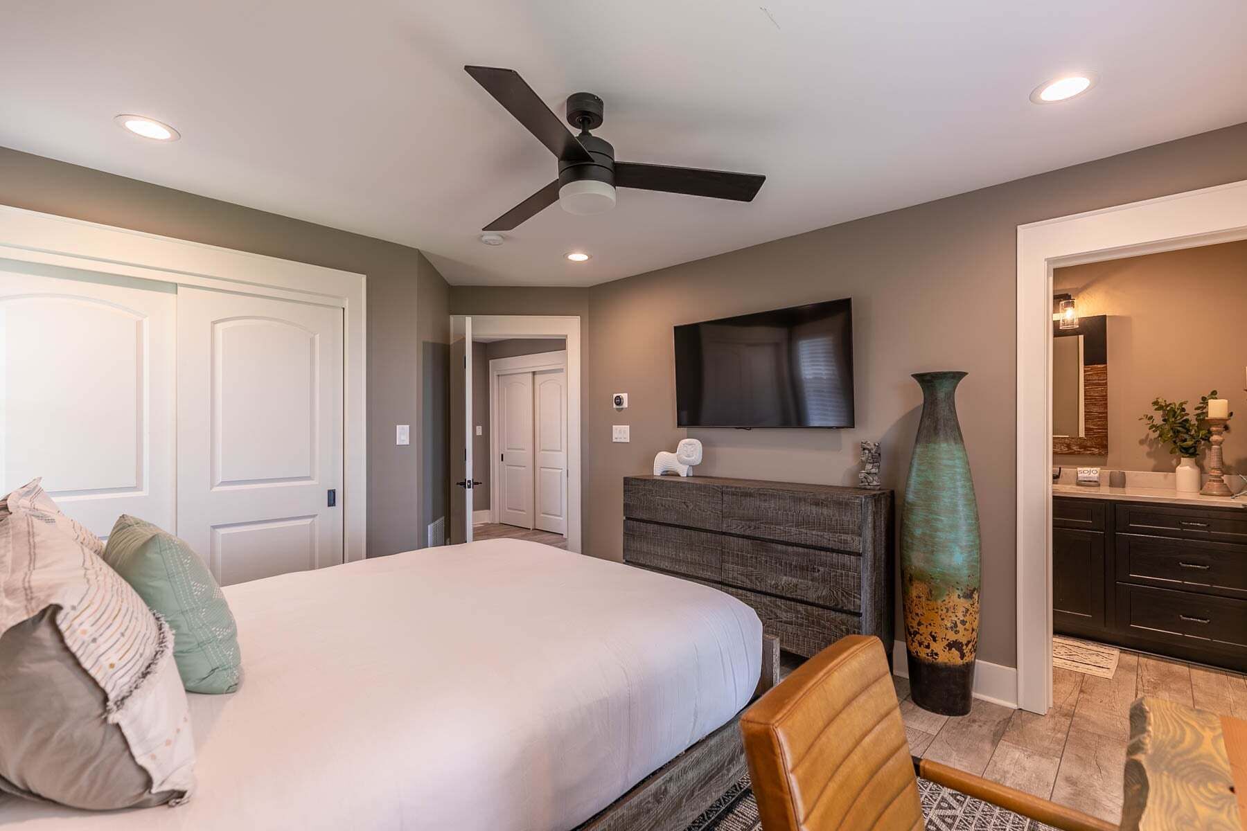 Une chambre à coucher avec un lit, une commode, un téléviseur, un grand vase et un ventilateur de plafond.