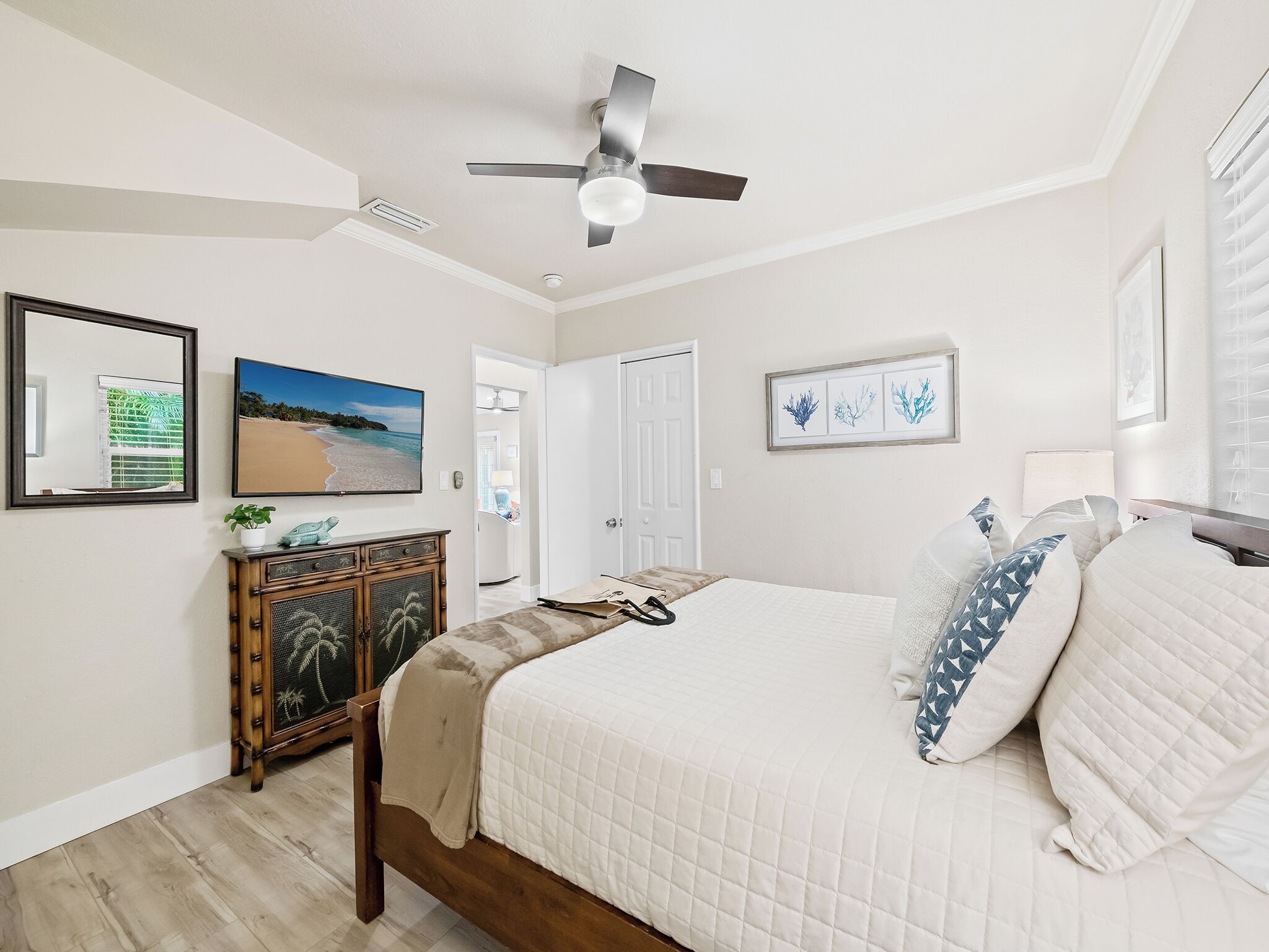A bedroom with a bed, a ceiling fan, a dresser, a TV, and framed artwork on the wall.