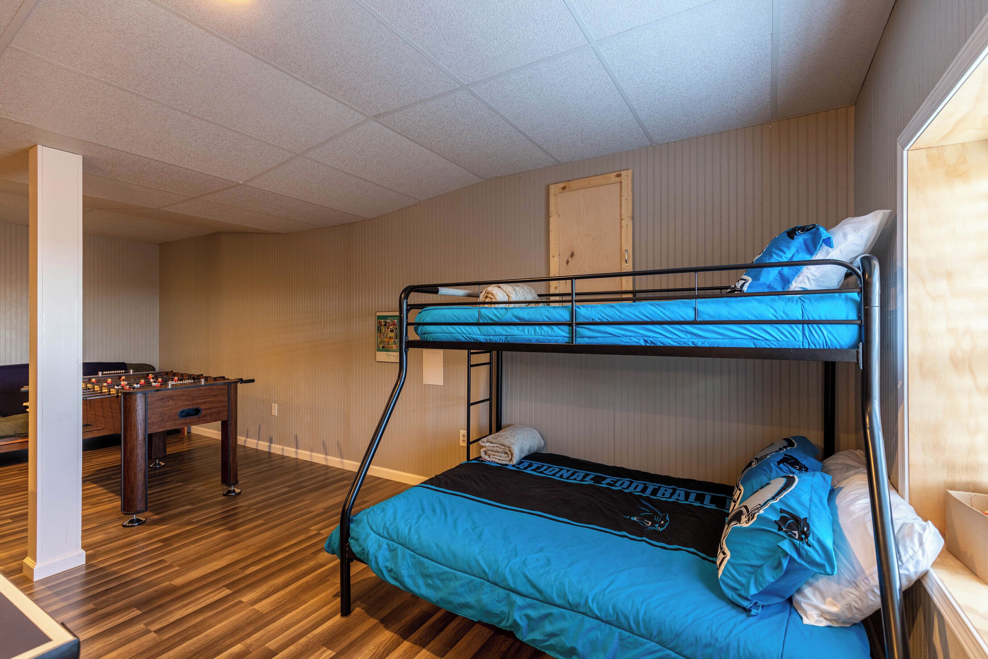 A bunk bed with blue bedding, a foosball table, and a wooden floor.