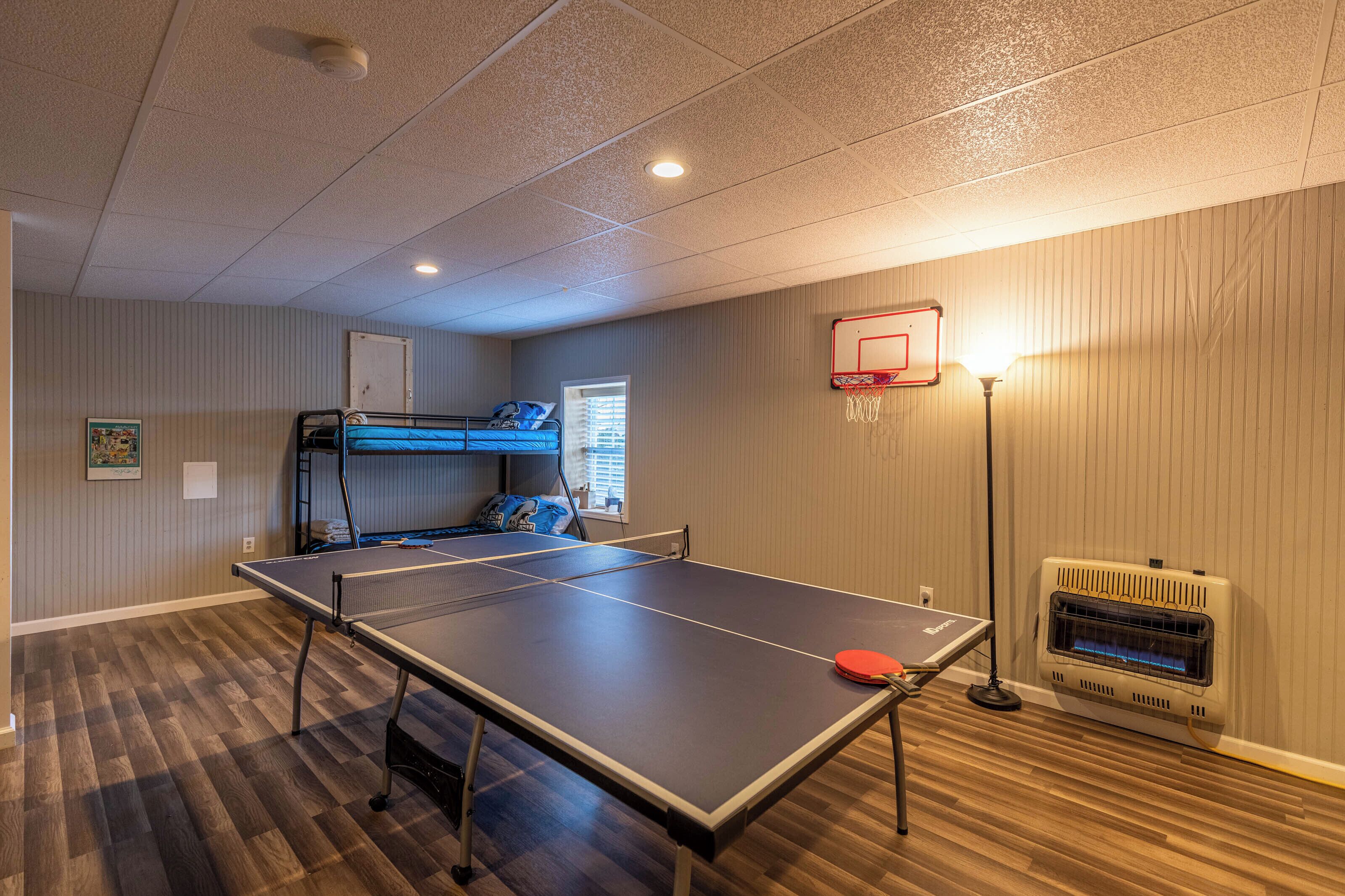 A room with a ping pong table, bunk beds, a basketball hoop, and a heater.