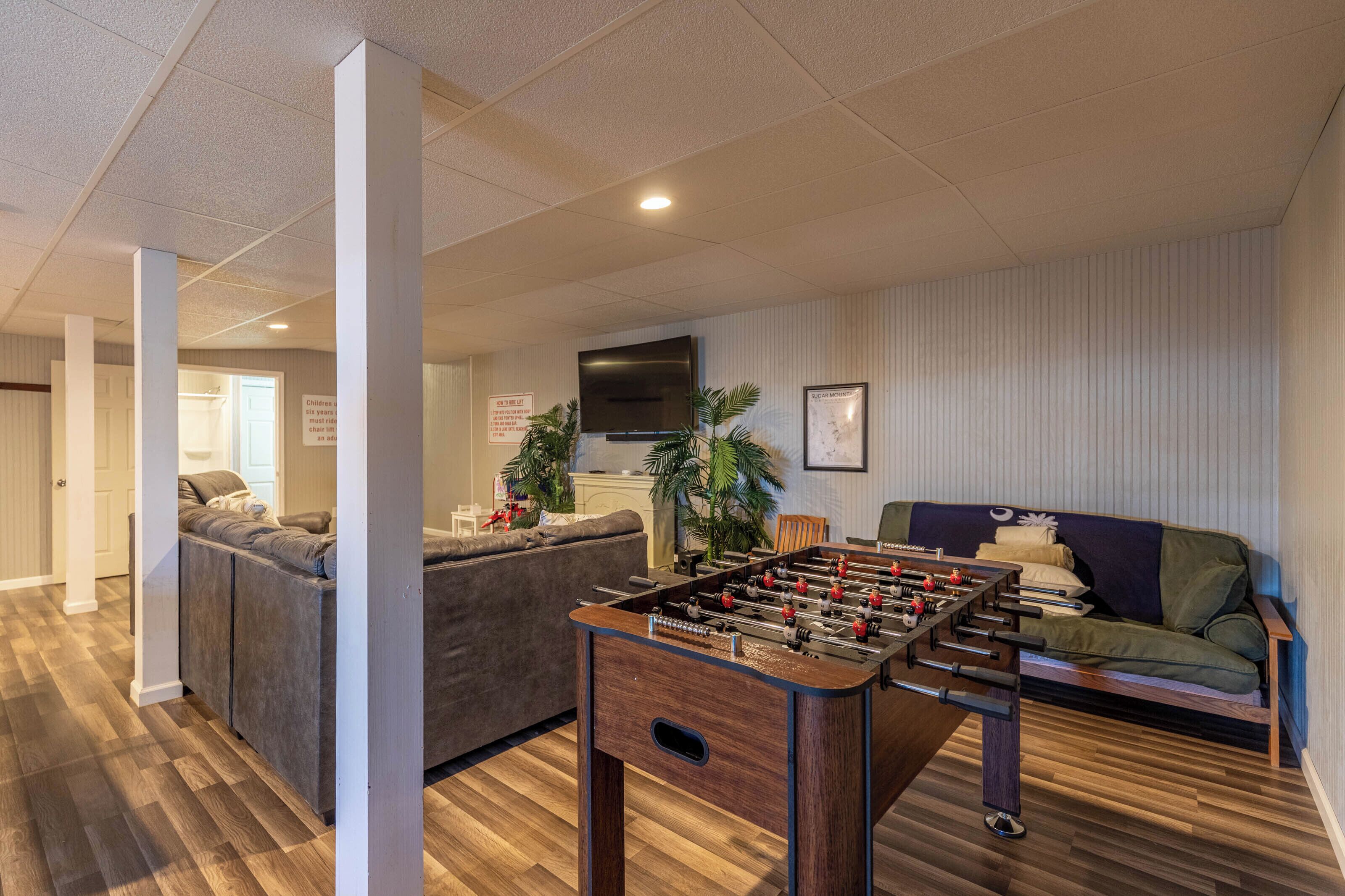 A room with a foosball table, a sofa, a television, and a door leading to another room.
