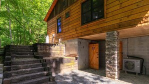 A wooden cabin with a stone staircase, a time room door, and an air conditioning unit. - Whiskey Creek Cabin Peaceful Creekside Cabin With hot tub and Game Room (Sugar Grove)