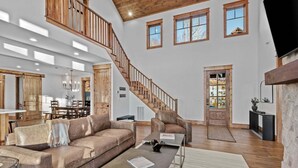 A spacious living area with a high ceiling, a wooden staircase, a dining area, and a cozy seating arrangement.