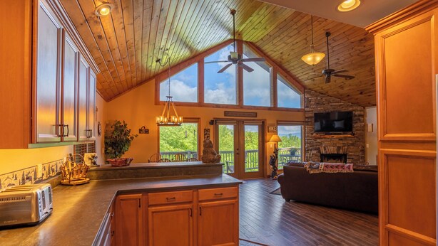 A spacious kitchen with a large island, wooden ceiling, and a stone fireplace. - Bearadise Cabin - Pet Friendly, Great Views, Firepit and Yard on Sugar Mountain, 2 Car Garage (Banner Elk)