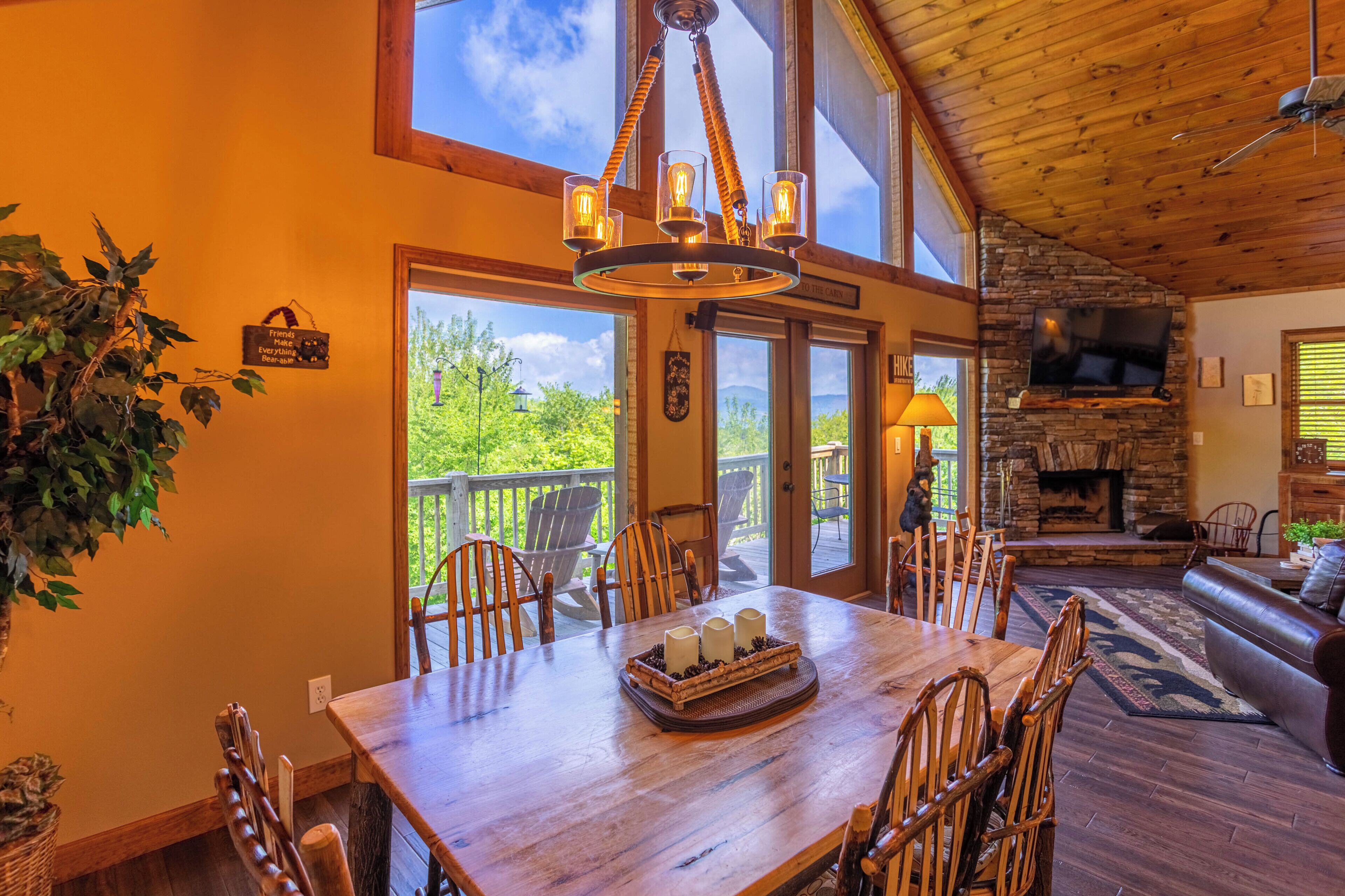 A wooden dining table with chairs, a chandelier, a stone fireplace, and a television mounted on the wall.