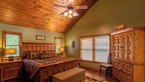 A bedroom with a wooden ceiling, a large bed, a wooden nightstand, a bench, a cabinet, and a ceiling fan. - Bearadise Cabin - Pet Friendly, Great Views, Firepit and Yard on Sugar Mountain, 2 Car Garage (Banner Elk)