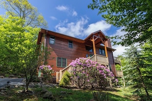 Une cabane en bois dotée d’un balcon, entourée d’une végétation luxuriante et d’arbustes en fleurs.
