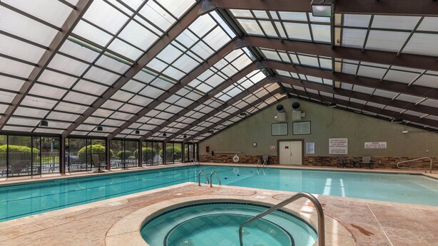 Una piscina interior con techo de vidrio, un jacuzzi y suelo de baldosas de piedra.