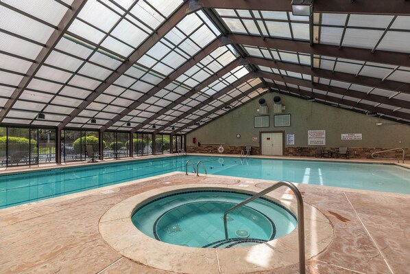 An indoor swimming pool with a glass ceiling, a hot tub, and a stone-tiled floor.