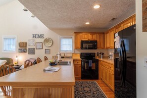 A kitchen with wooden cabinets, a black refrigerator, a microwave, and a dining area with a table and chairs.