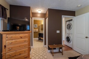 A laundry room with a washing machine, a television on a wooden dresser, and a small table.