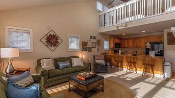 A spacious living room with a green sofa, a coffee table, and a kitchen area with wooden cabinets and a bar.