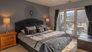 Un dormitorio con cama, dos mesitas de noche, ventilador de techo y vistas a un espacio exterior a través de una puerta corrediza de vidrio.