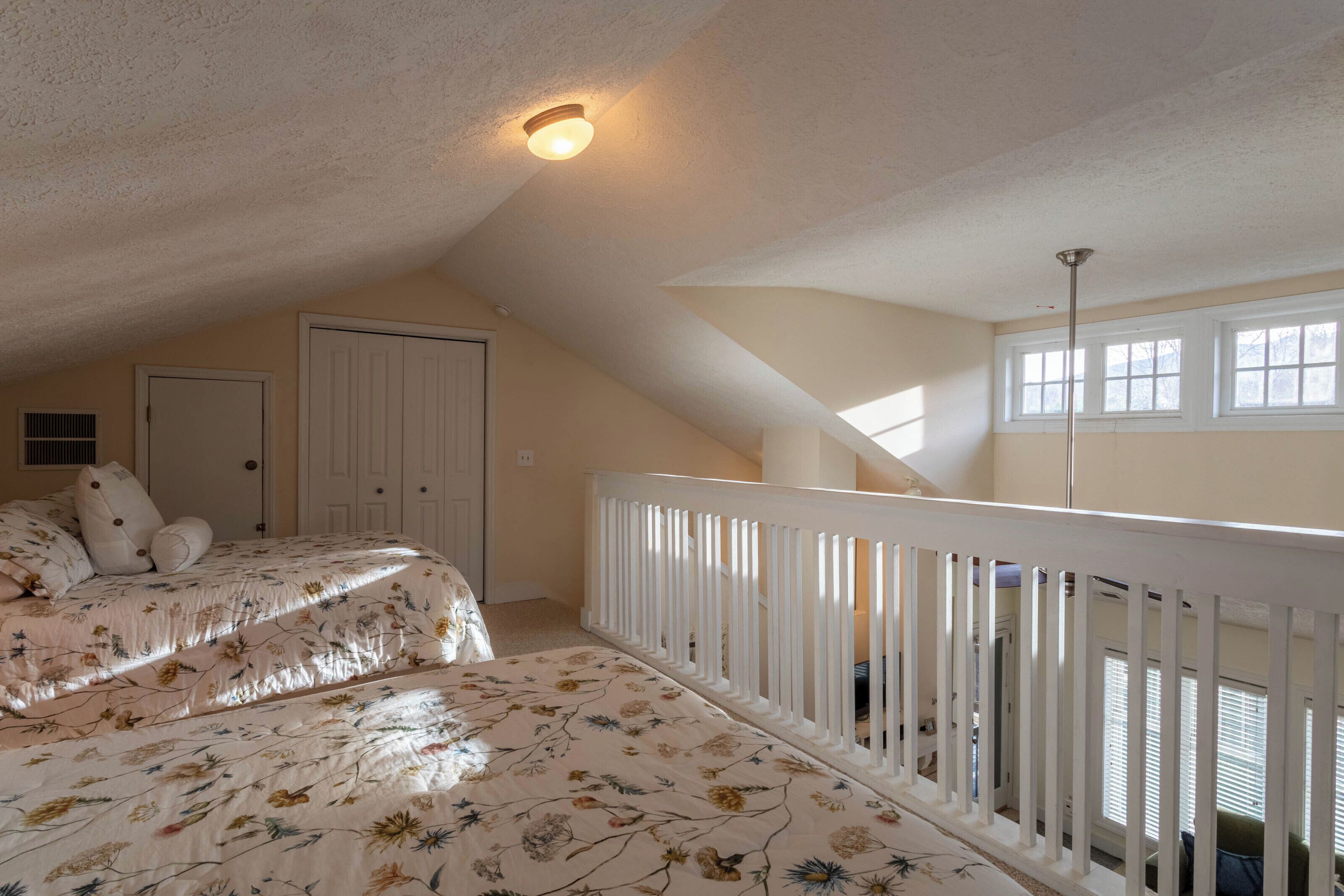 A bedroom with two beds, a white railing, a door, and a window.