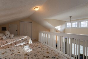 A bedroom with two beds, a white railing, a door, and a window.