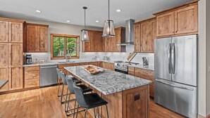 A modern kitchen with wooden cabinets, stainless steel appliances, a marble island, and bar stools. - Grandview Pointe (Banner Elk)