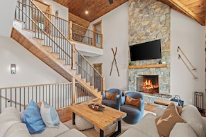 A modern living room with a stone fireplace, a flat-screen TV, and a wooden staircase.
