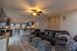 Ein geräumiges Wohnzimmer mit einer dunkelbraunen Ledersofa, Zebra-Muster-Pouffen und einem Deckenventilator.